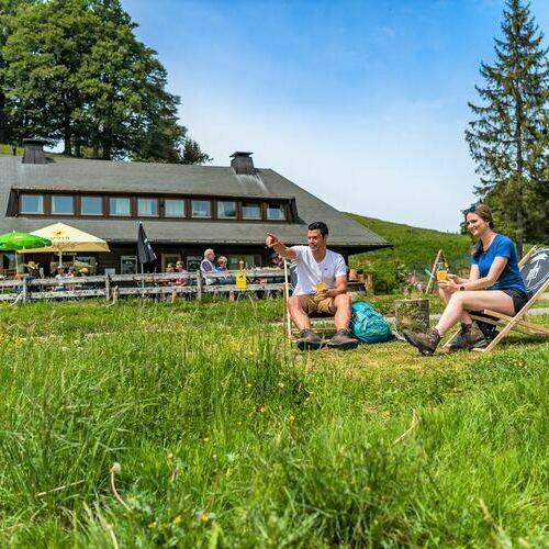 Ein Paar sitzend vor dem Almgasthaus Knpflesbrunnen. Beide genieen den Ausblick sowie ein Getrnk. 